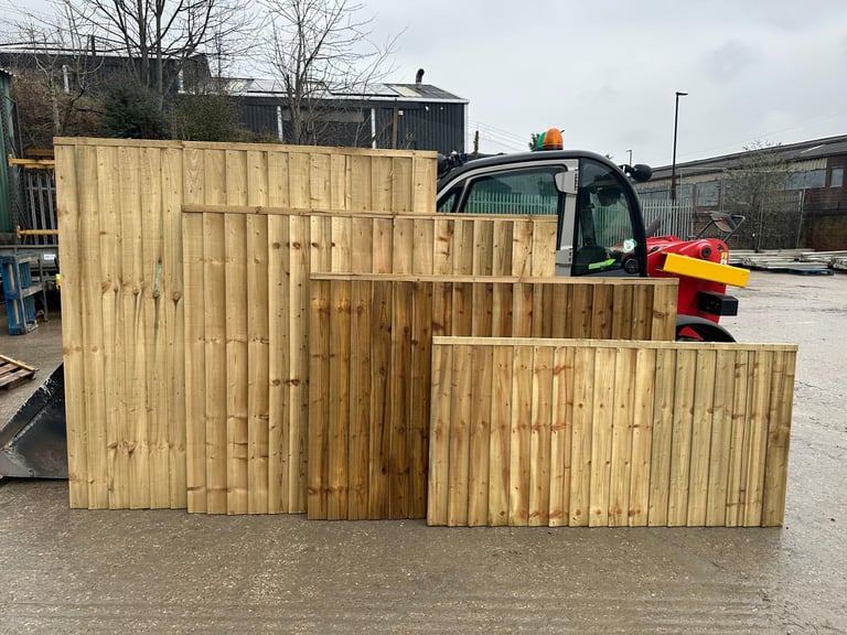Stacked wooden fence panels of varying heights displayed in an industrial yard